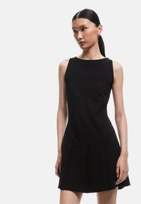 Musta hihaton mekko, joka on valmistettu sileästä kankaasta. Mekossa on tiukka bodice ja keinokuituinen hame, jossa on laskoksia. Minimalistinen muotoilu, ei näkyviä kuvioita.