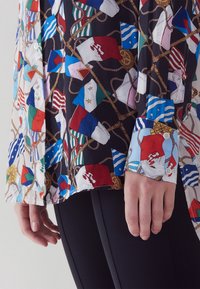 Kraagshirt van lichtgewicht, multikleurig stof met een patroon van nautische vlaggen, met een zwarte basis en knoopsluiting bij de manchetten.