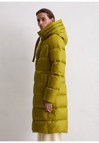 Lange, puffige parka in olijfgroen met een hoge kraag en een verstelbare kap. Heeft horizontale gestikte secties en elastische manchetten.