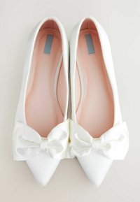 Ballerines en satin blanc avec un embout pointu et un grand nœud à l'avant, présentant un intérieur rose et une texture lisse.