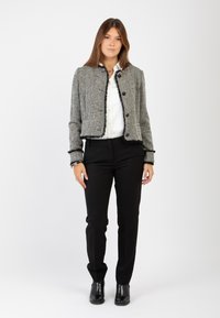 Giacca cropped in tweed grigio con rifiniture in frange nere, dotata di bottoni rotondi. Abbinata a pantaloni neri su misura e stivaletti.
