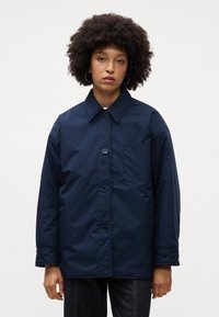 Giacca button-up blu navy con colletto a punta, una tasca sul lato sinistro del petto e polsini elasticizzati per una vestibilità comoda.