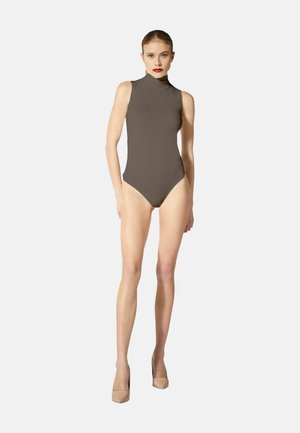 Donna in body color tortora senza maniche con collo alto e tacchi beige su uno sfondo chiaro uniforme.