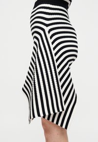 Μαύρη και λευκή ριγέ πλεκτή φούστα με ψηλή μέση, ασύμμετρη γραμμή τελειώματος και υφή υφάσματος. Διαθέτει στενές και φαρδιές ρίγες σε όλο το μήκος.