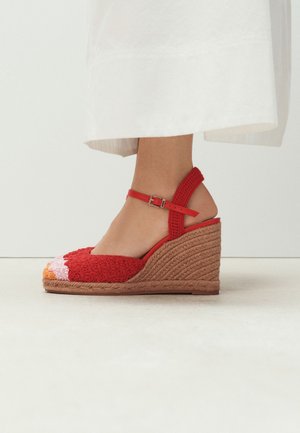 Kileformet espadrillesandal med rød hæklede overdel, ankelrem og naturflettet platåsål, båret med hvid nederdel.