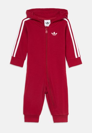 Czerwony kombinezon dla niemowlaka z kapturem, zamkiem z przodu, białym logo Adidas na piersi i białymi paskami na obu długich rękawach.