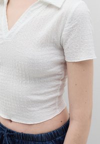Witte top met korte mouwen, een subtiel textuurpatroon, V-hals en een aansluitende pasvorm, gecombineerd met denim shorts met trekkoord.