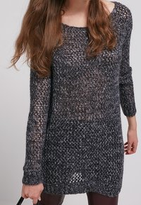 Långärmad, löst sittande tröja i mörkgrått, med en texturerad, öppen stickdesign. Rundad halsringning och ribbade ärmslut.