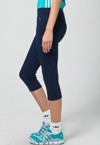 Marina beskurna leggings gjorda av stretchigt tyg, med sidostreck och hög midja. Kombinerat med turkosa träningsskor och vita strumpor.