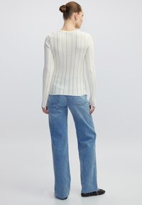 Weißes, geripptes Langarmtop mit rundem Halsausschnitt, kombiniert mit hellblauen, weit geschnittenen Jeans, die einen lässigen Schnitt und Stil zeigen.
