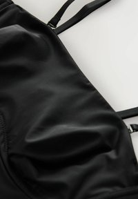 Zwarte zwemtop gemaakt van glad, ondoorzichtig stof. Voorzien van verstelbare banden en een gestructureerd ontwerp met subtiele stikdetails.