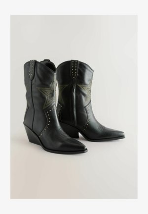 Fekete bőr cowboy csizmák hegyes orral, wedge sarkú, csillagmintával, arany szegecsekkel és oldalsó cipzárral. Textúrált felület.