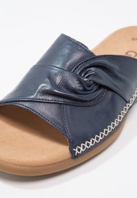 Sandale ouverte en cuir bleu marine avec un design noué et une couture blanche en croix sur une semelle rembourrée couleur tabac et une semelle extérieure en caoutchouc.
