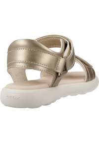 Sandali metallici dorati con più cinturini, dotati di una soletta imbottita e una suola in gomma bianca. Etichettati "Geox" sulla suola.