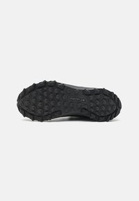 Semelle de chaussure de randonnée en caoutchouc noir avec des crampons profonds et des motifs hexagonaux pour une meilleure adhérence, avec le logo Columbia au centre.