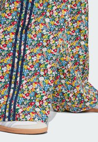 Floral-patterned wide-leg pants in blue, featuring multicolored flowers. Navy stripes adorn the sides. Accompanied by light-colored footwear.