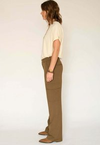 Haut beige clair à manches courtes assorti à un pantalon cargo marron taille haute avec poches latérales. Modèle portant des ballerines marron. Design simple.