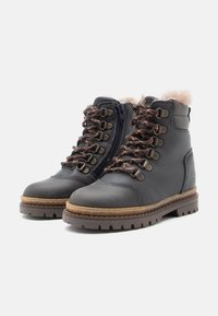 Bottes en cuir bleu marine avec col en fourrure, œillets en métal et lacets marron. Présentent une fermeture éclair sur le côté et une semelle en caoutchouc texturée pour une meilleure adhérence.