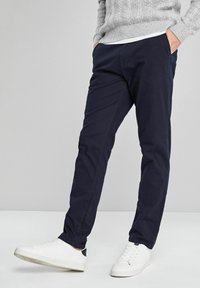 Tummansininen puuvillachino-housut, joissa on slim fit -leikkaus, sivutaskut ja sileä pinta, yhdistettyinä valkoisiin lenkkareihin.