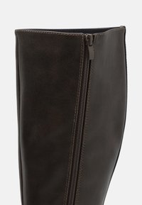 Botte en cuir marron jusqu'au genou, dotée d'une fermeture éclair latérale, avec une texture lisse et des coutures contrastantes le long de la couture. Pas d'embellissements supplémentaires.