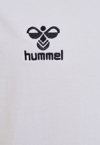 Hvid t-shirt med sort broderet "hummel" logo og bi-design. Blød bomuldsstruktur med enkle, rene linjer.
