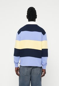 Bawełnowy sweter z kolorowym blokiem, w którym znajdują się jasnoniebieskie, żółte i granatowe paski. Posiada okrągły dekolt i długie rękawy.