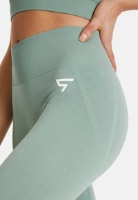Mint green high-waisted leggings made of stretchy fabric with a ribbed waistband, featuring a white logo on the side and textured design.