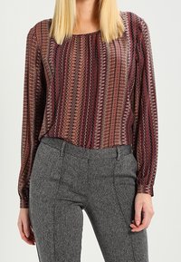 Camicia a maniche lunghe a fantasia nei toni del borgogna, grigio e crema, con scollatura rotonda, abbinata a pantaloni grigi a trama con cuciture frontali.