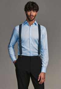 Light blue dress shirt with a button-down collar, textured fabric, paired with dark suspenders and black tailored pants.