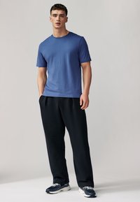 Kék rövid ujjú póló, laza szabású, fekete bő fazonú nadrággal párosítva. A lábbeli tengerészkék és fehér színű mintázattal rendelkezik.