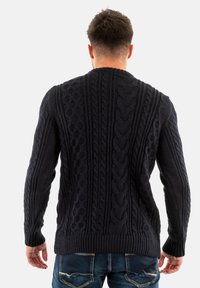 Jersey de punto trenzado en color marino con puños y dobladillo acanalados, presentando un patrón texturizado en la parte posterior. Hecho de hilo suave y grueso.