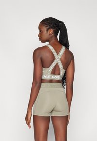Sujetador deportivo atlético de color verde olivo con diseño de espalda cruzada y letras en blanco "NIKE PRO", combinado con pantalones cortos ajustados a juego. Textura suave.