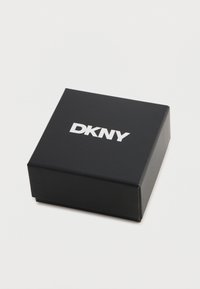Črni pravokotni zaboj s mat površino, z izstopajočim belim logotipom "DKNY" na vrhu. Tekstura površine, čist dizajn.
