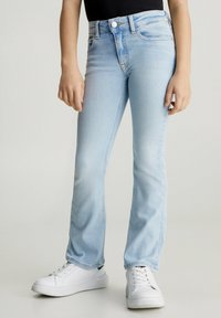 Jeans in denim azzurro chiaro con un taglio dritto, dotati di un bottone e zip, cinque tasche e una leggera sbiaditura. Abbinati a sneaker bianche.