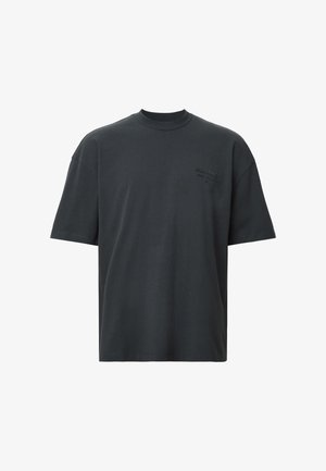 Camiseta de algodón negra con cuello redondo, mangas cortas y detalle de logo en relieve en la parte frontal. Textura suave y corte relajado.