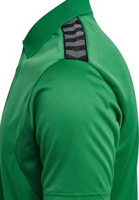 Grøn polo skjorte med struktureret stof, krave og sort accent på nakken bagpå med et mønstret design.