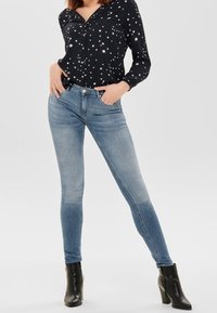 Tajta jeans i ljusblå denim med en urtvättad finish, tillsammans med en svart blus med stjärnmönster och svarta högklackade stövlar.