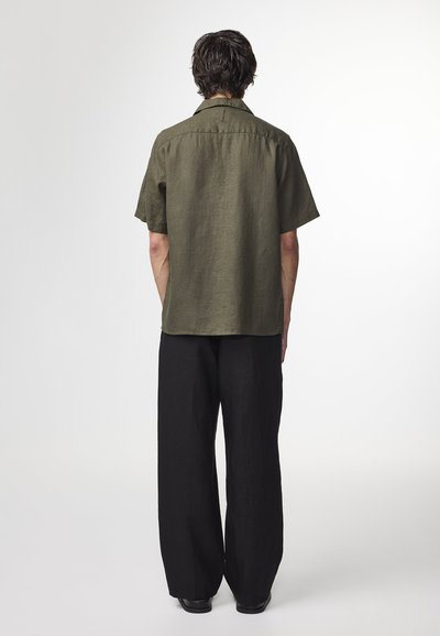 Kortärmad, olivgrön linne skjorta med krage, i kombination med svarta vida byxor. Slät textur, minimalistisk design.