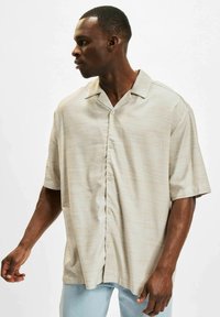 Beige kortermet skjorte med et subtilt stripete mønster, knappefront og skjortekrage. Stoffet ser glatt og lett ut.