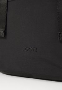 Borsa in tessuto nero con una texture liscia. Il nome del marchio "JOOP!" è scolpito in un colore nero abbinato sul fondo.