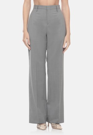 Pantaloni grigi a vita alta e gamba larga indossati da una persona in piedi con tacchi beige appuntiti con dettagli ritagliati.