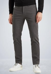 Graue Slim-Fit-Hosen aus einem Baumwollmischgewebe, mit einer glatten Textur, vorderen Taschen und dezenten Nähdetails. Kombiniert mit weißen Sneakers.
