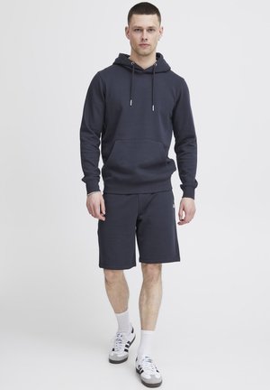 Dark gray hoodie with a kangaroo pocket, drawstrings, and ribbed cuffs, paired with matching shorts, and white footwear with black accents.