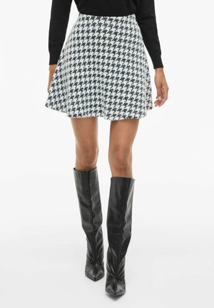 Minirok van een wolmix in zwart-wit houndstoothpatroon, uitlopende stijl met een zoomlijn boven de knie. Gecombineerd met glanzende zwarte laarzen tot de knie.
