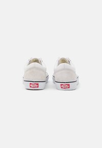 Bílé a světle šedé semišové tenisky s nízkým designem, gumovou podrážkou a červeným logem Vans na zadní straně. Čistý, minimalistický styl.
