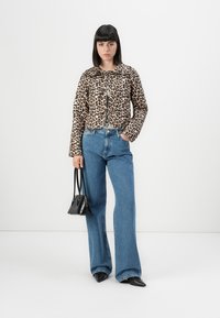 Leopardmönstrad kort jacka, raka blå denimjeans, svarta spetsiga skor och en liten svart handväska. Slät textur och djärvt mönster.
