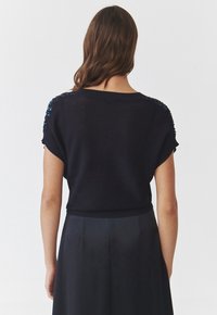 Top tricotat negru cu mâneci scurte, având accente texturate pe umeri. Designul include un decolteu larg și o lungime scurtă.