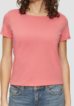 T-shirt z krótkim rękawem, okrągłym dekoltem w kolorze koralowym, wykonany z miękkiej bawełny. Posiada luźny krój i podwinięte mankiety rękawów. Zestawiony z niebieskimi dżinsami.