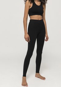 Zwarte sportoutfit bestaande uit een strakke crop top en hooggekapte legging, gemaakt van een rekbaar materiaal met een gladde textuur.
