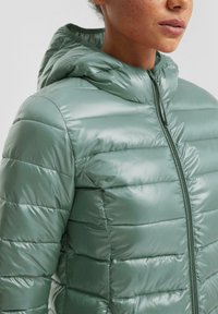 Chaqueta acolchada con capucha en material brillante de color verde claro; cuenta con un cierre de cremallera recto y un patrón de acolchado horizontal para aislamiento.